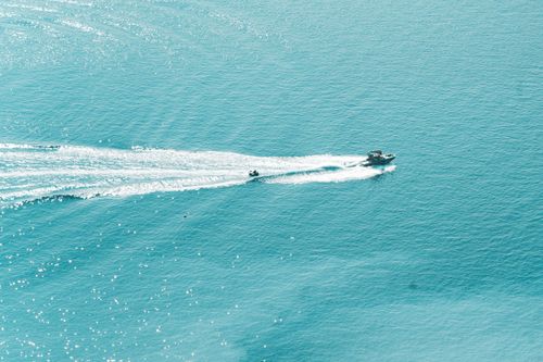 Free A speedboat glides across the tranquil, turquoise sea, leaving a dramatic wake behind. Stock Photo