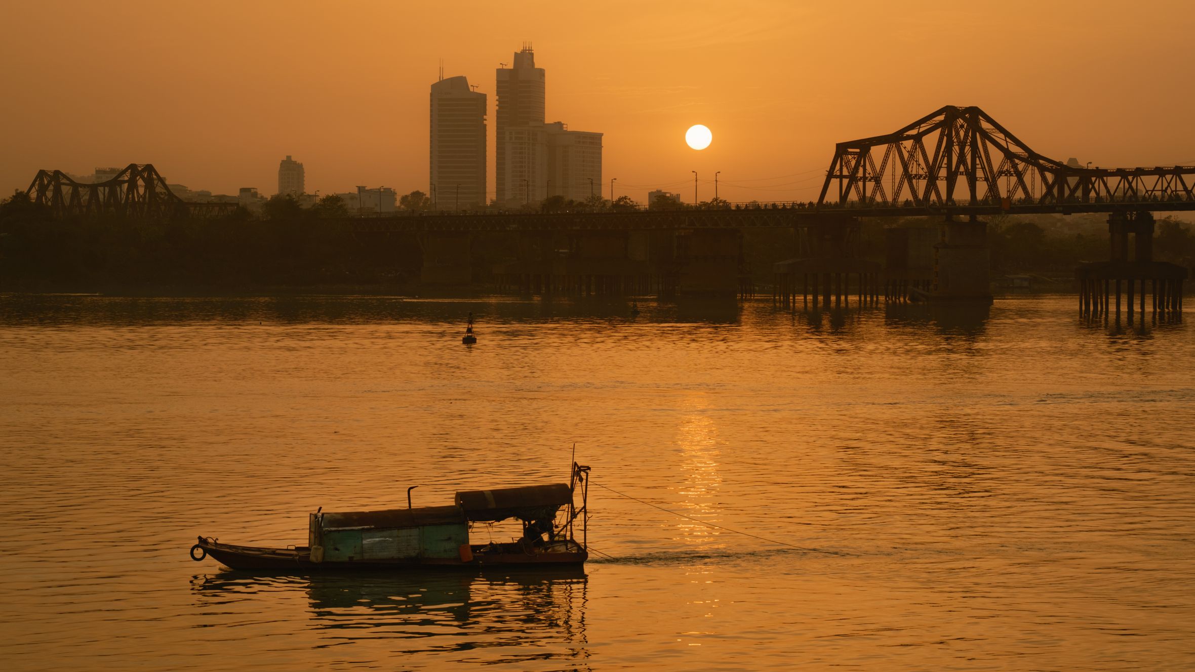 Tranquil sunset view of Long Bien Bridge in Hanoi with a boat on the river.