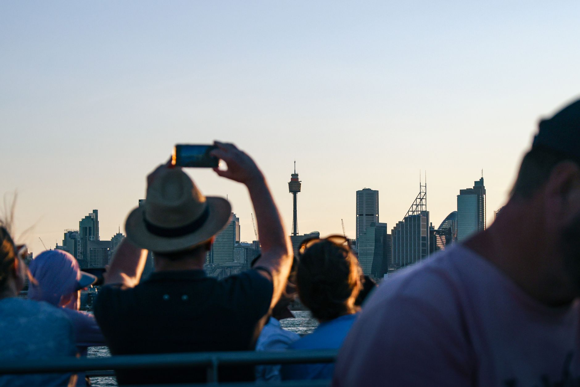 Tourists photograph the Sydney skyline from a boat during sunset. Iconic city view.