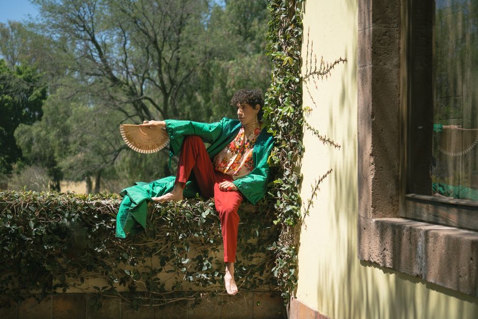 A person in vibrant clothing sits outdoors with a traditional fan, exuding elegance.