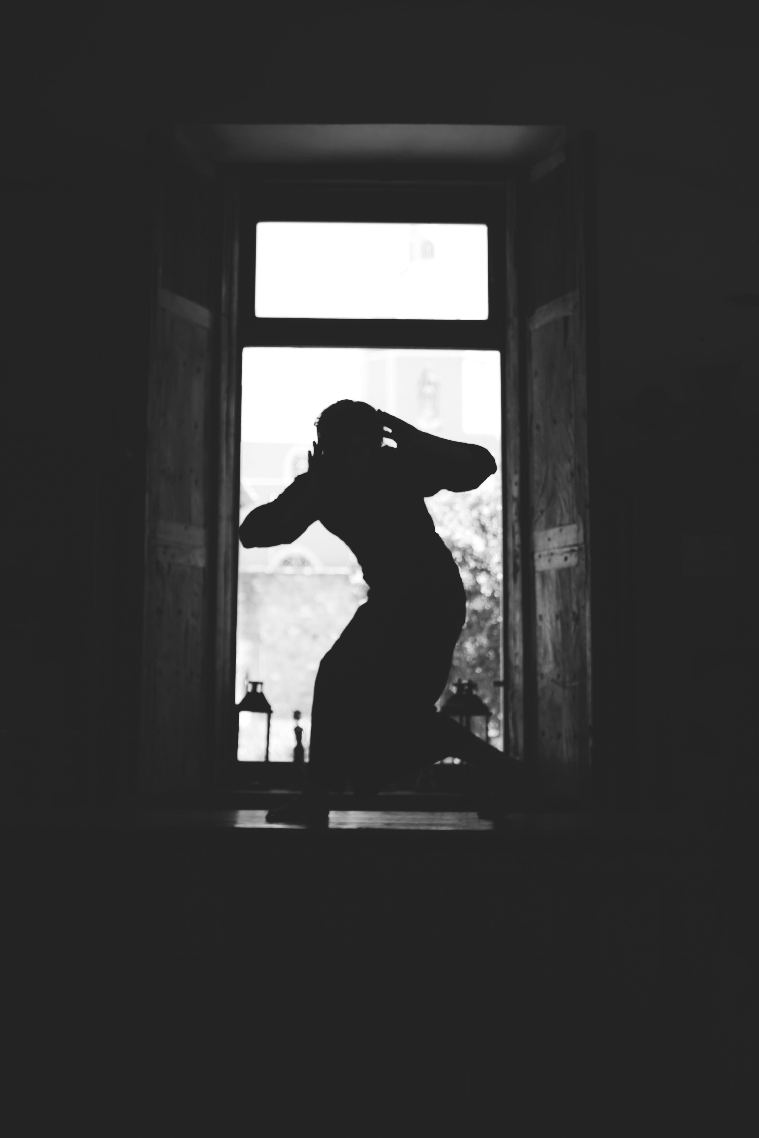 gratis Een dramatisch zwart-wit silhouet van een persoon die creatief poseert in een raamkozijn. Stockfoto