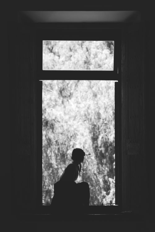 Free Artistic silhouette of a woman sitting by a window, captured in black and white, creating a mysterious and thoughtful mood. Stock Photo