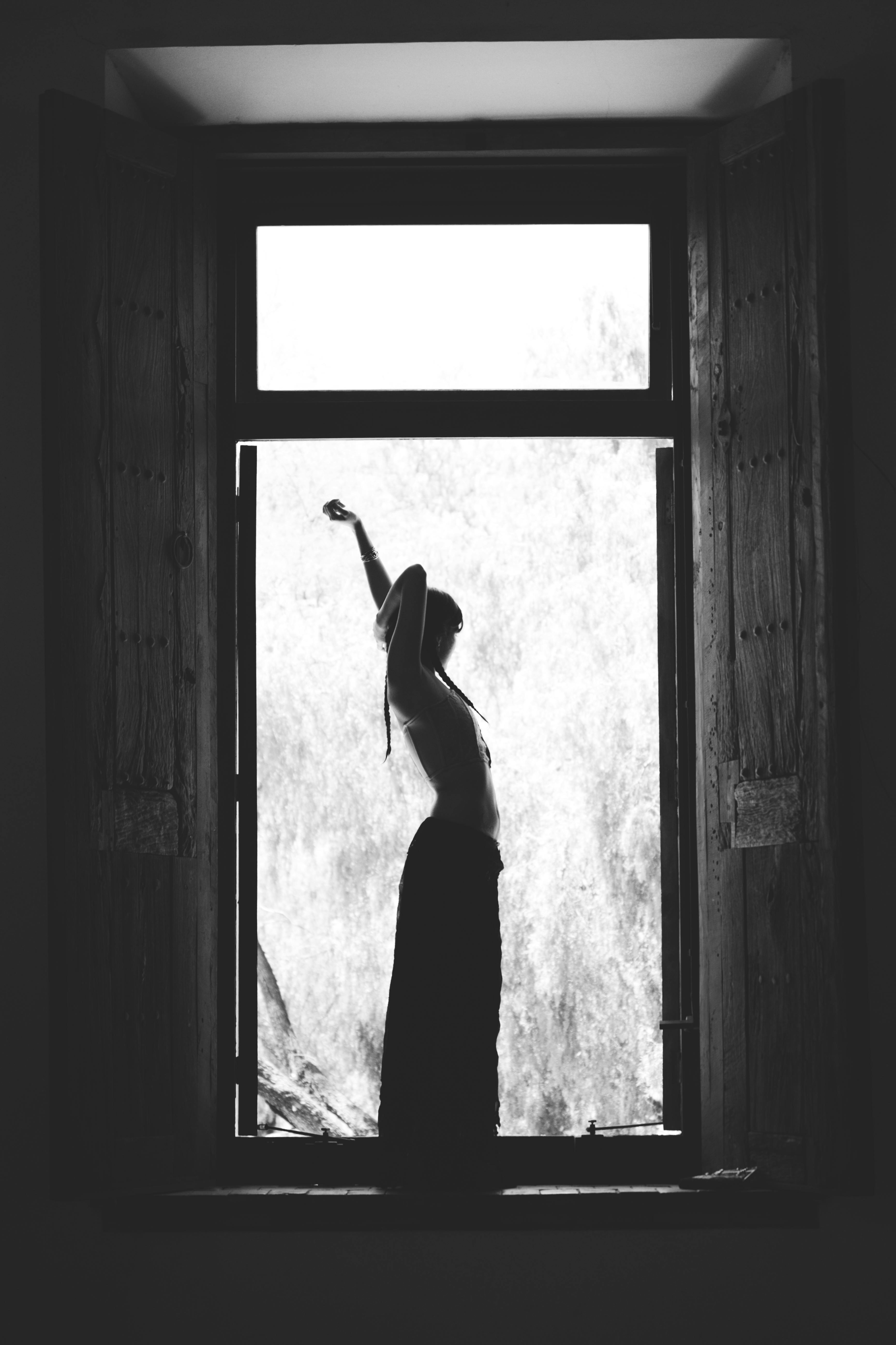 A striking black and white silhouette of a woman posing in a window frame, capturing elegance and contrast.