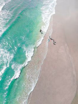 A stunning aerial view of children playing by turquoise waves on a sunny beach.