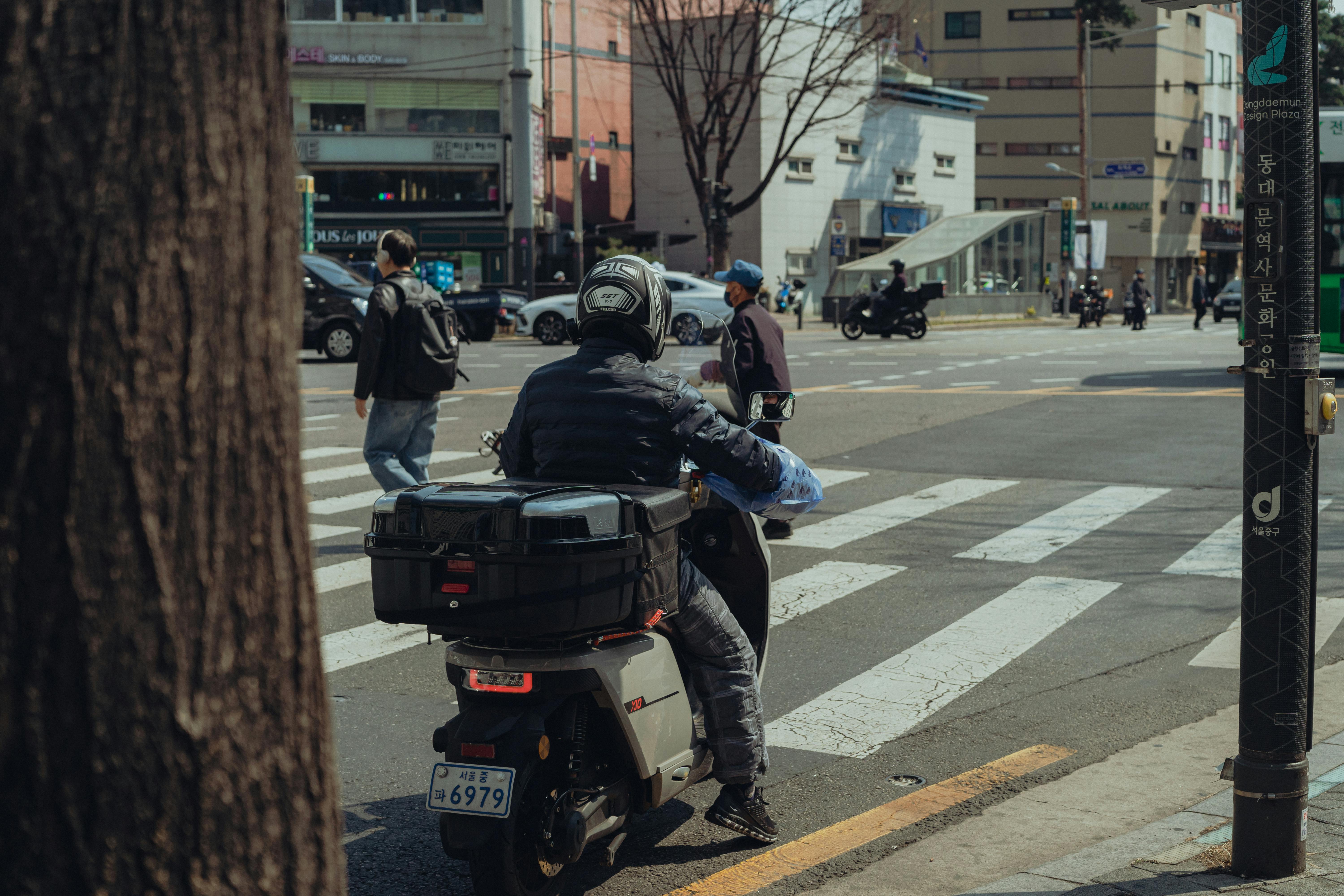A busy street intersection in Seoul, South Korea, featuring a scooter and pedestrians crossing.