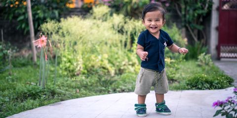 Happy toddler taking steps outdoors in a vibrant garden setting.