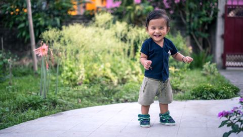 Happy toddler taking steps outdoors in a vibrant garden setting.