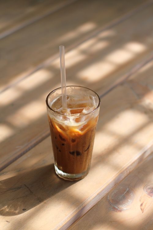 Free Glass of iced coffee on a wooden table, bathed in soft sunlight, creating a refreshing summer vibe. Stock Photo