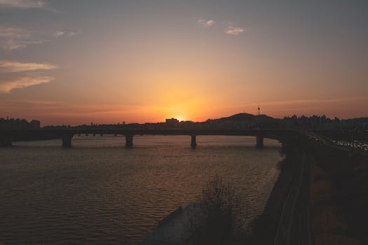 A stunning sunset view over a river with a bridge and city silhouette.