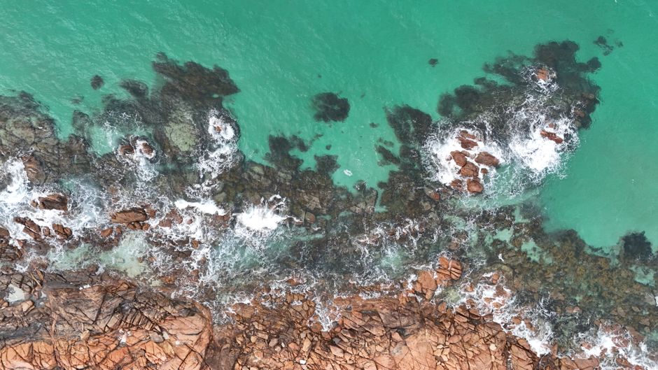 Stunning aerial shot of rugged Busselton coastline with turquoise waves crashing on rocks.