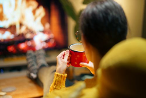 Free Woman relaxing with a hot beverage by the fireplace, enjoying a warm winter evening indoors. Stock Photo