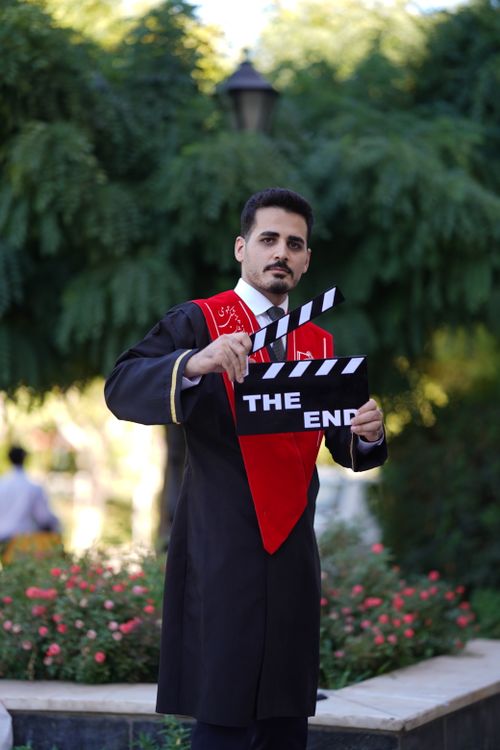 Free Graduate in traditional robe holding 'The End' clapperboard outdoors in Iran. Stock Photo