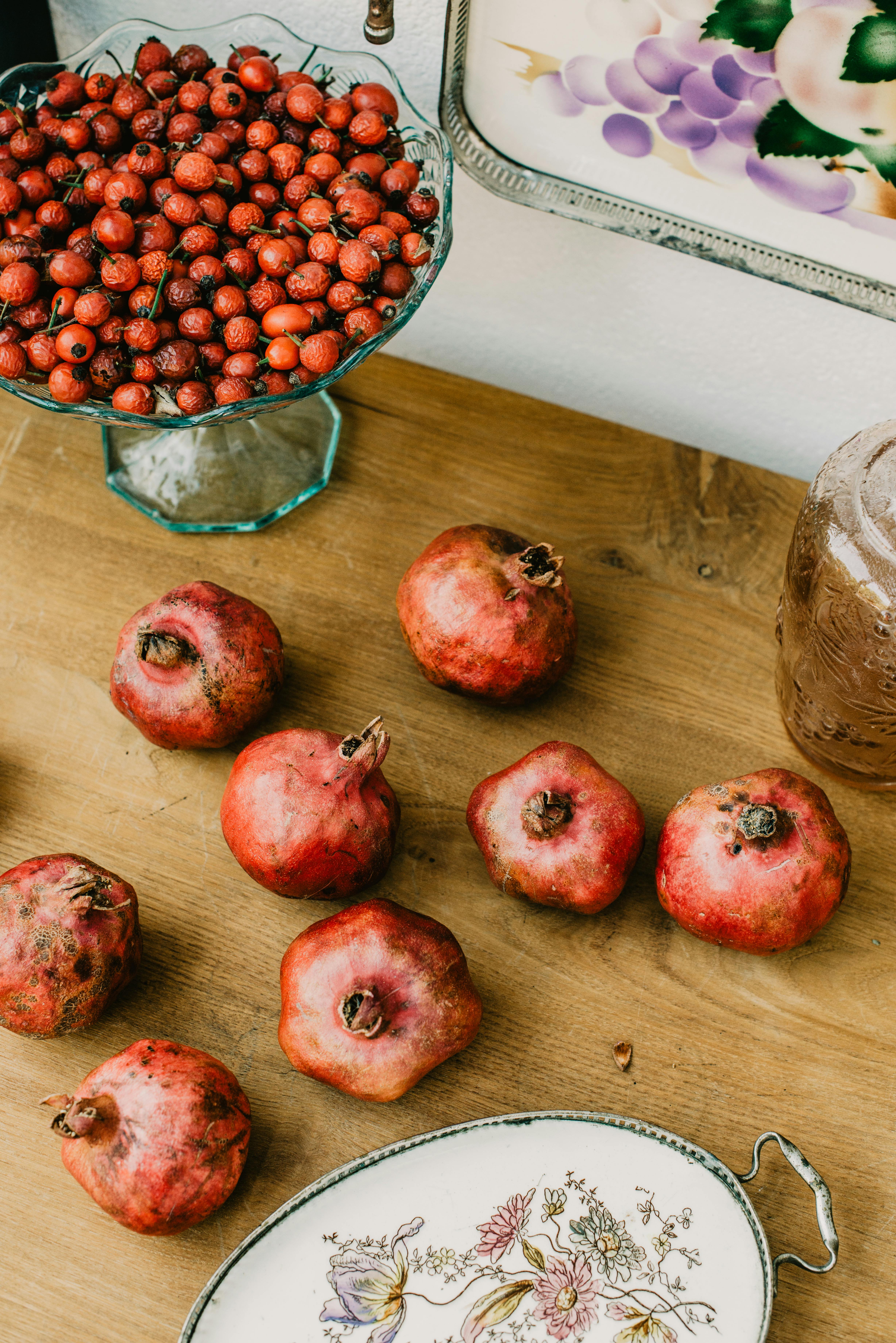 A rustic scene with fresh pomegranates and hawthorn berries displayed on a wooden table.