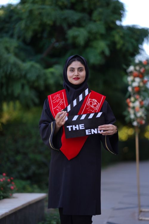 Free A young woman in traditional Iranian attire holds a graduation sign outdoors. Stock Photo