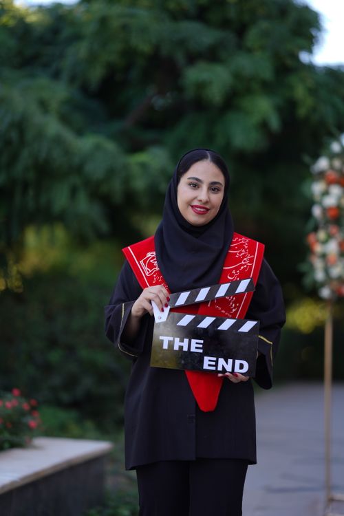 Free Young woman celebrating graduation outdoors with a ceremonial clapperboard. Stock Photo