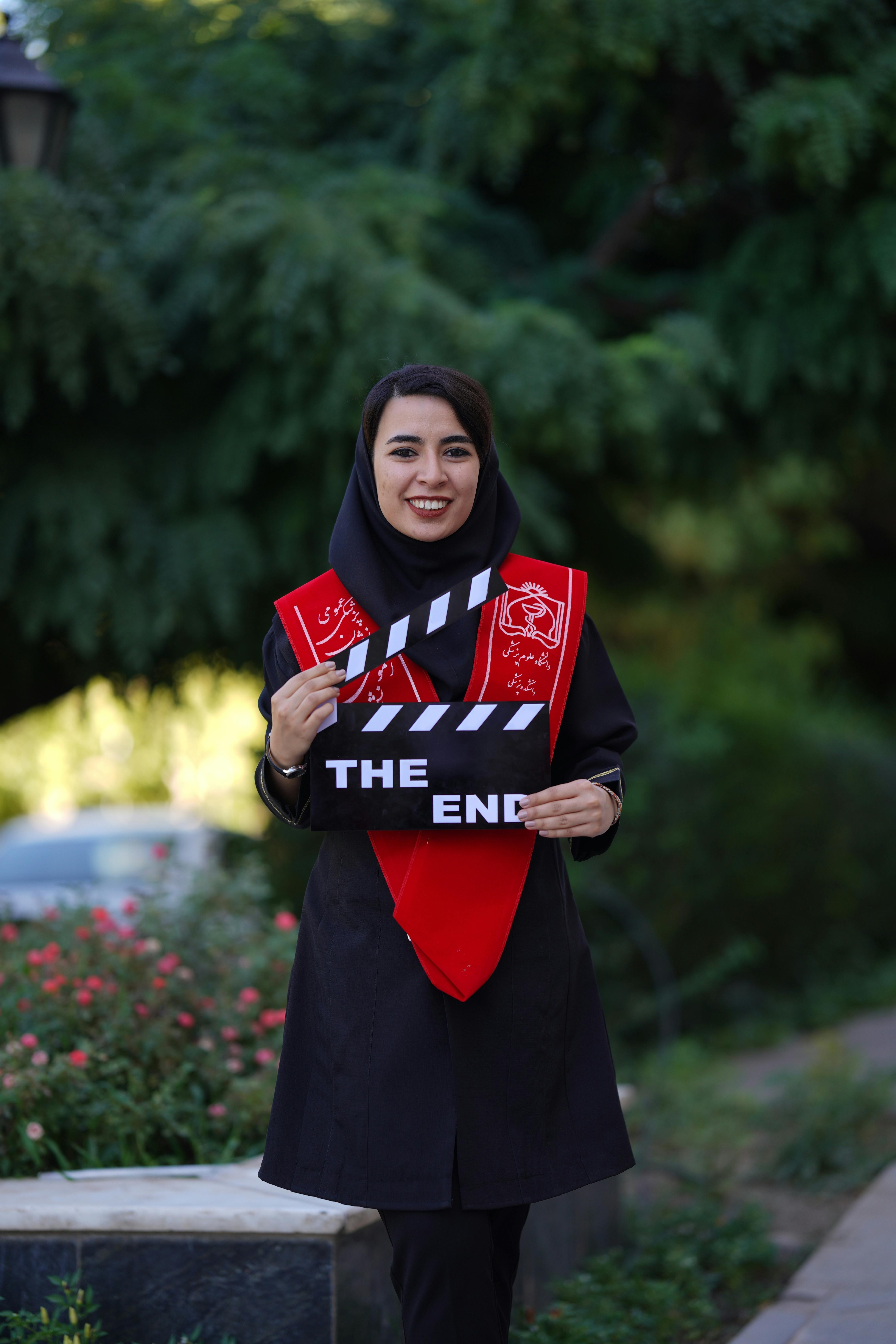 Smiling woman with hijab holding clapperboard outdoors, symbolizing film completion.
