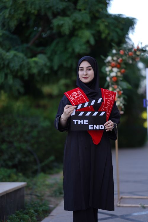 Free Young woman in graduation attire holding a clapperboard marked 'The End' in an outdoor setting. Stock Photo