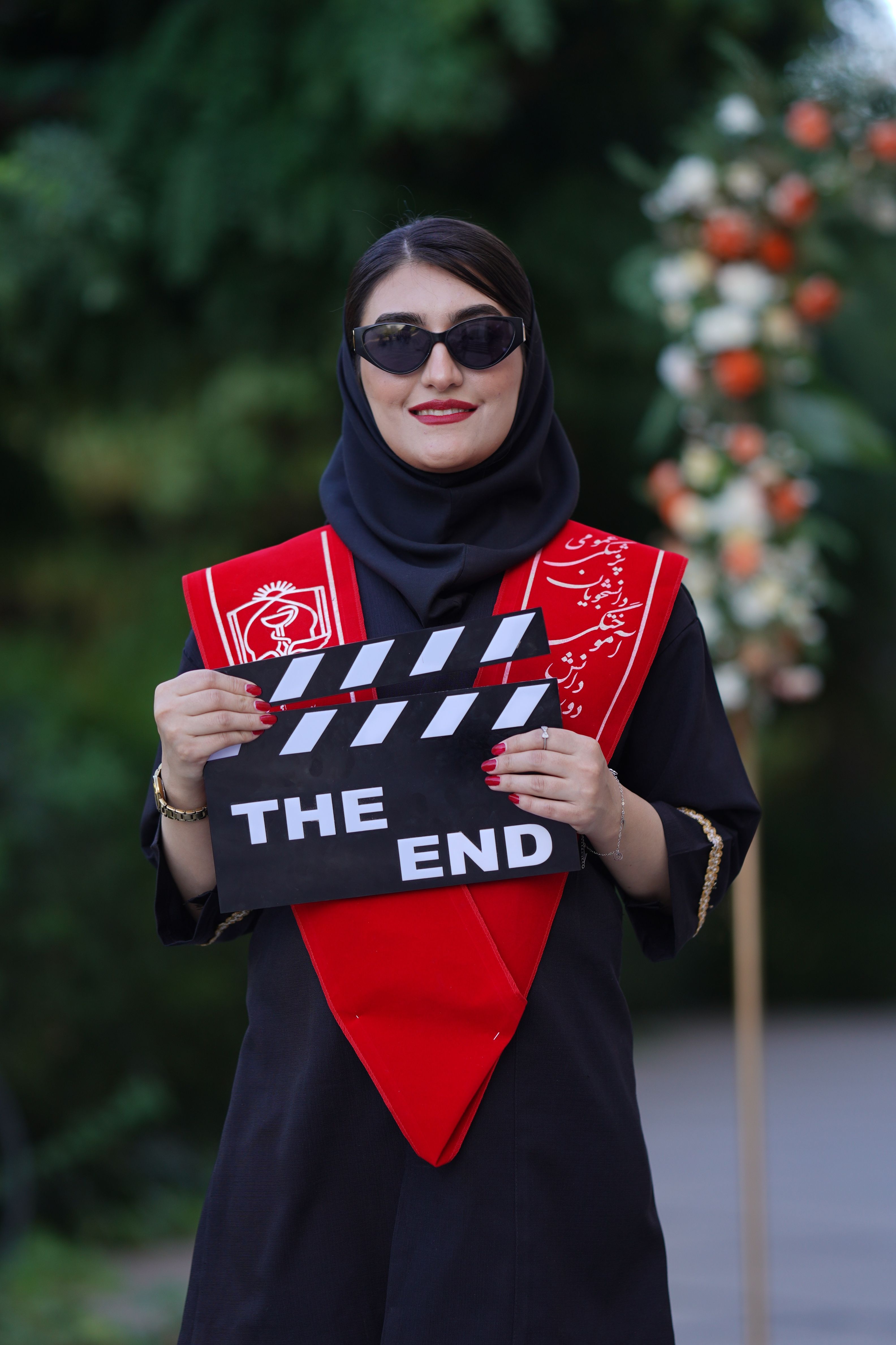 Portrait of a stylish Iranian woman holding a 'The End' clapperboard outside.