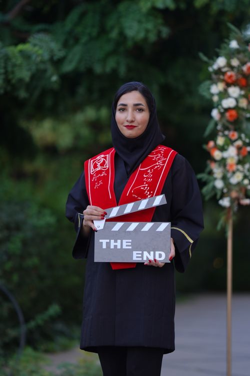 Free Middle Eastern woman in graduation attire holds a clapboard reading 'The End' symbolizing a significant achievement. Stock Photo
