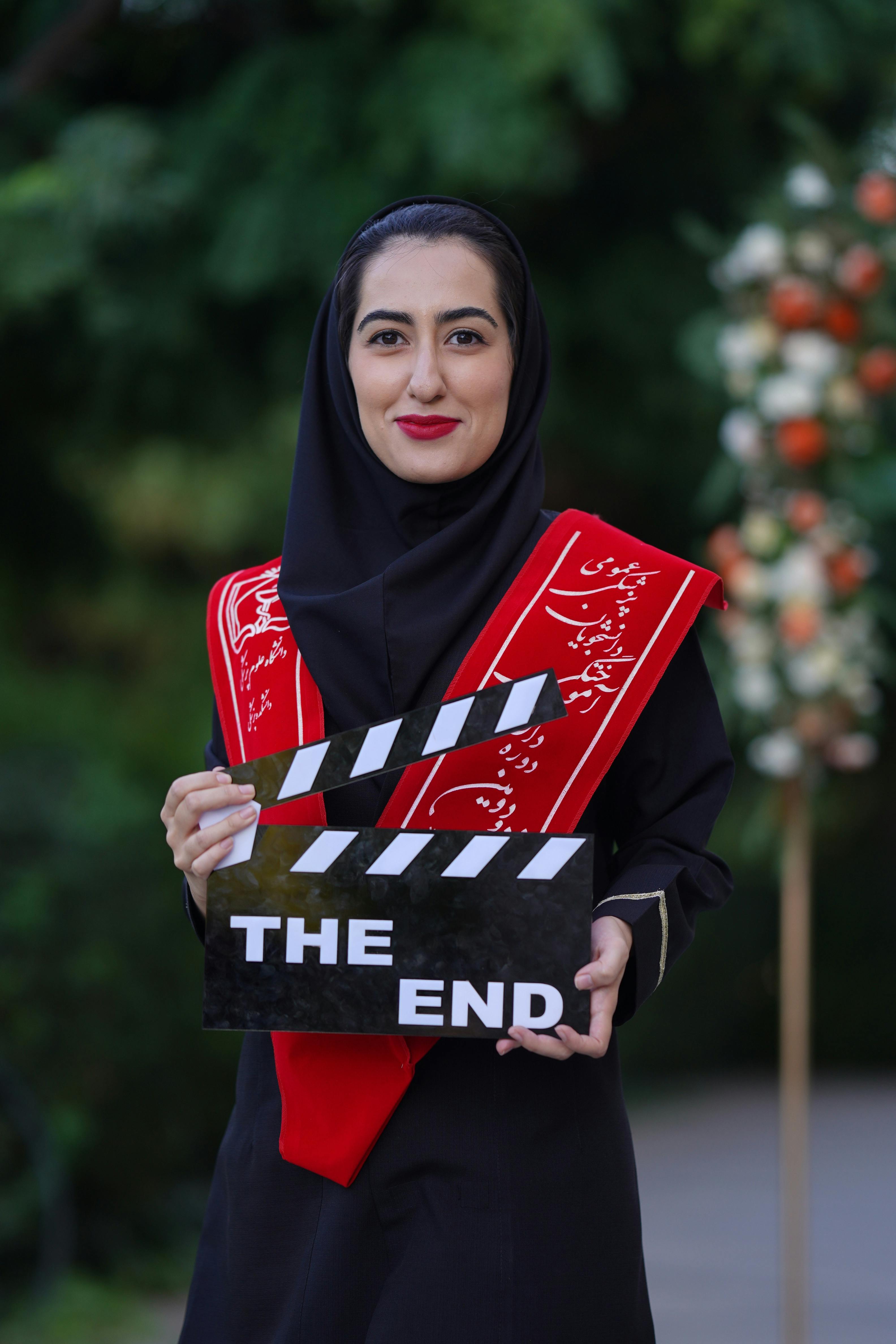 Woman in traditional attire holding a clapperboard with 'The End', outdoors.