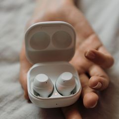 Hand holding an open white charging case with two round white earbuds inside