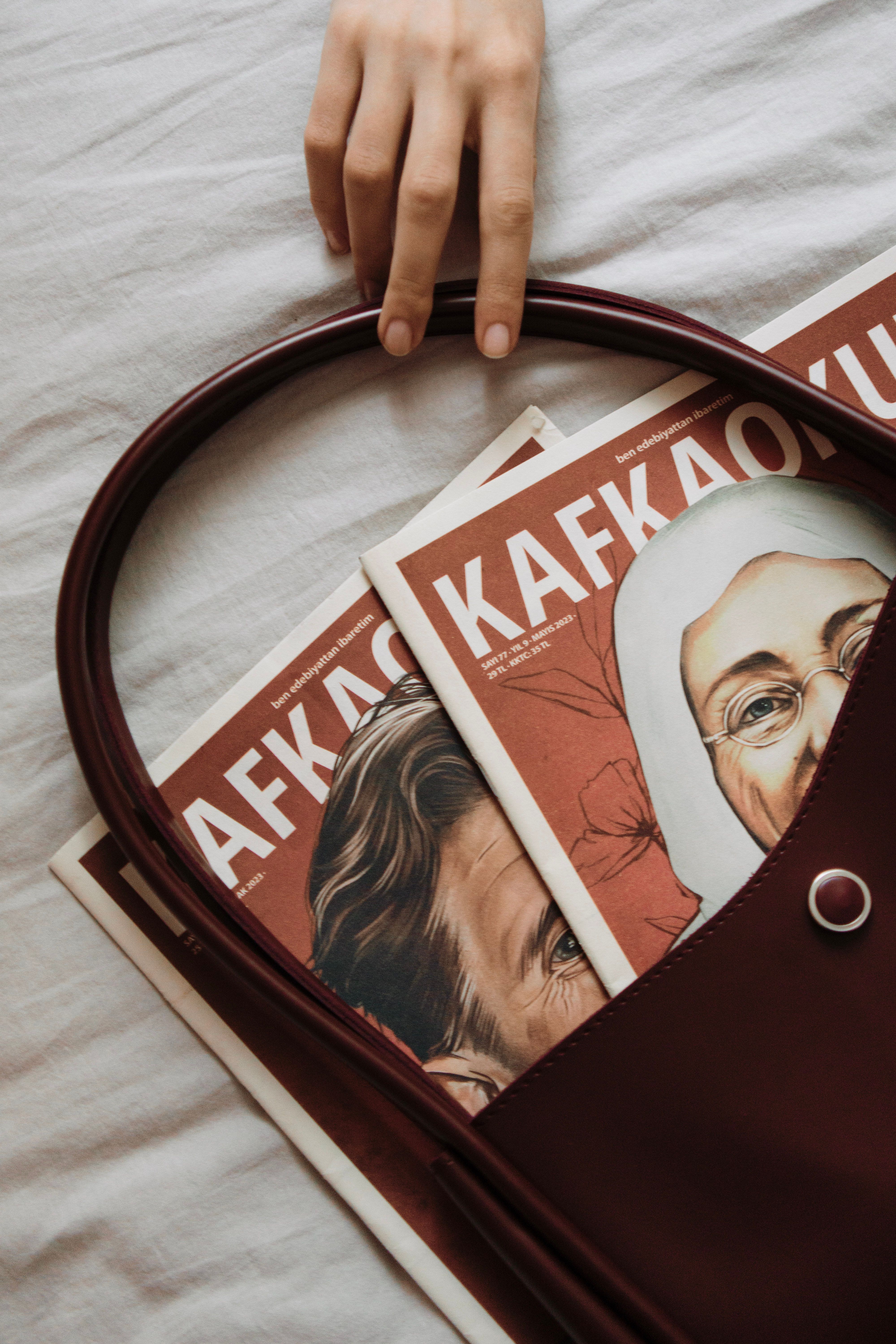 A hand reaches for a leather bag with magazines inside on a soft surface. Artistic and stylish composition.