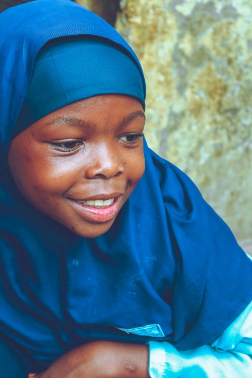 Free A young girl in a blue hijab smiles warmly against a textured background. Stock Photo