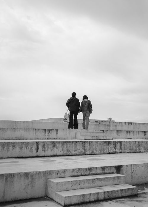 Free Two people walking on Durrës promenade under a cloudy sky. Black and white photography. Stock Photo
