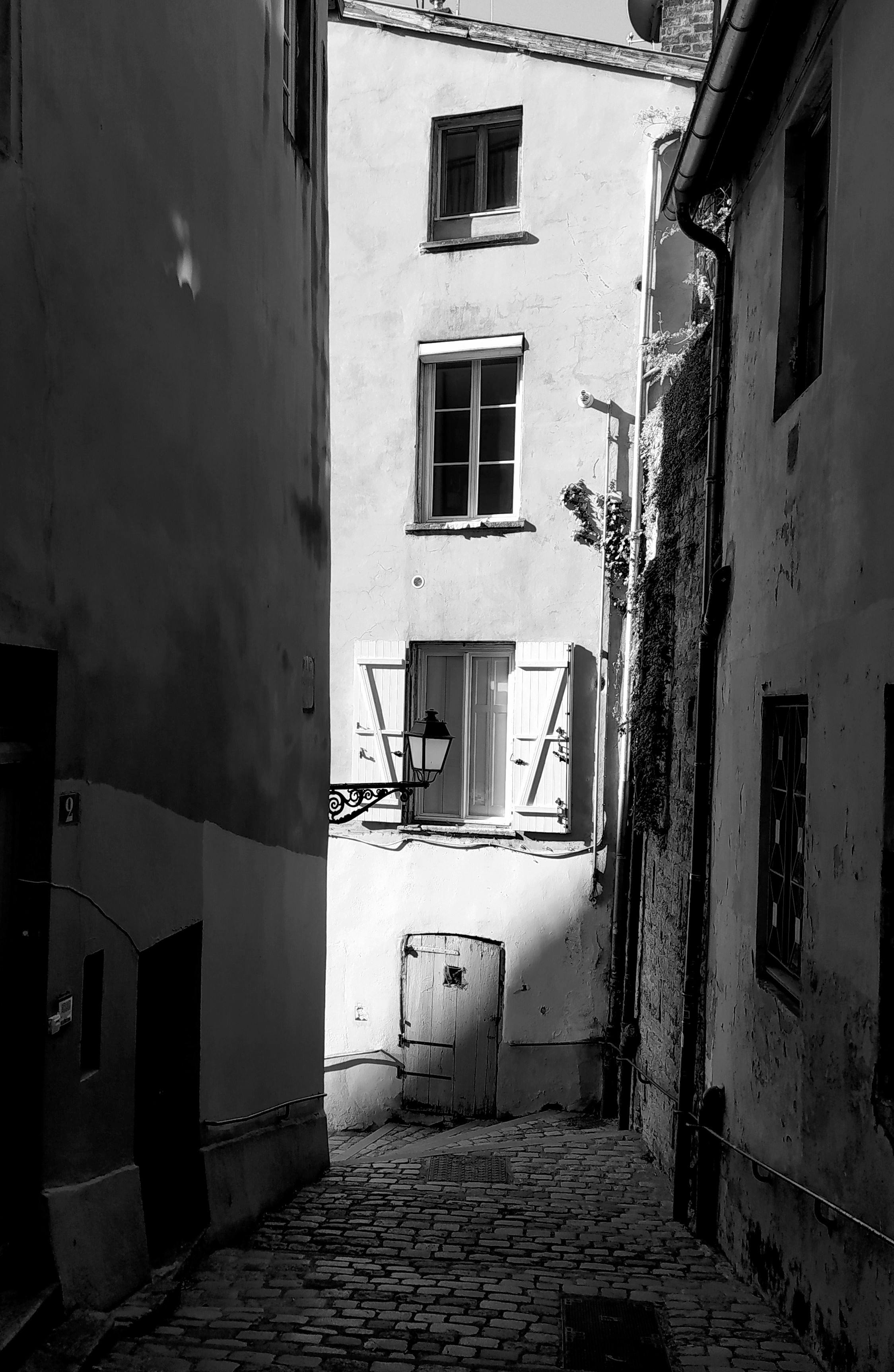 Black and white photo of a narrow alleyway in Lyon, France, showcasing historic architecture.