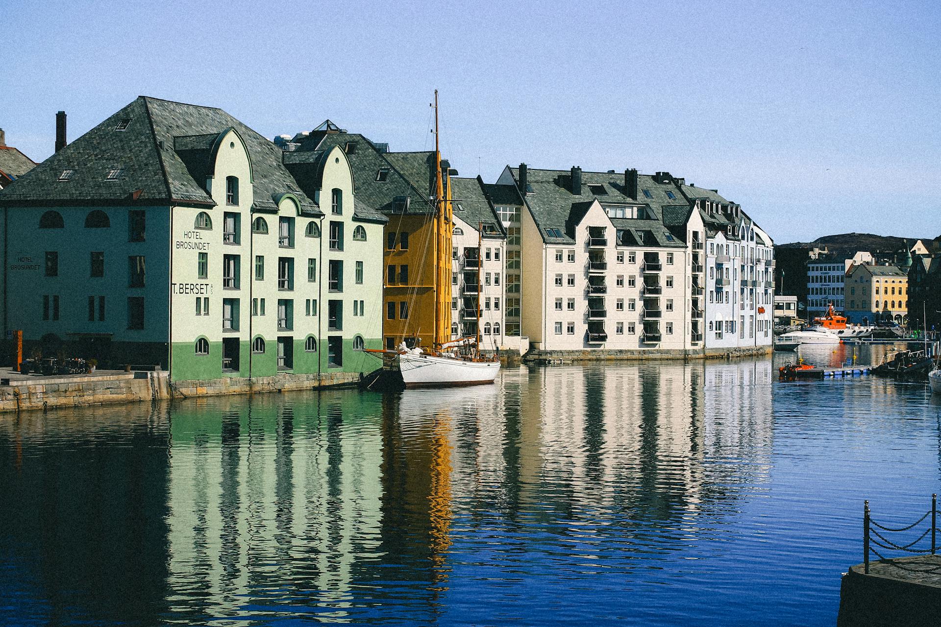 Colorful architectural buildings along the waterfront in Alesund, Norway, reflecting in the water under a clear sky.