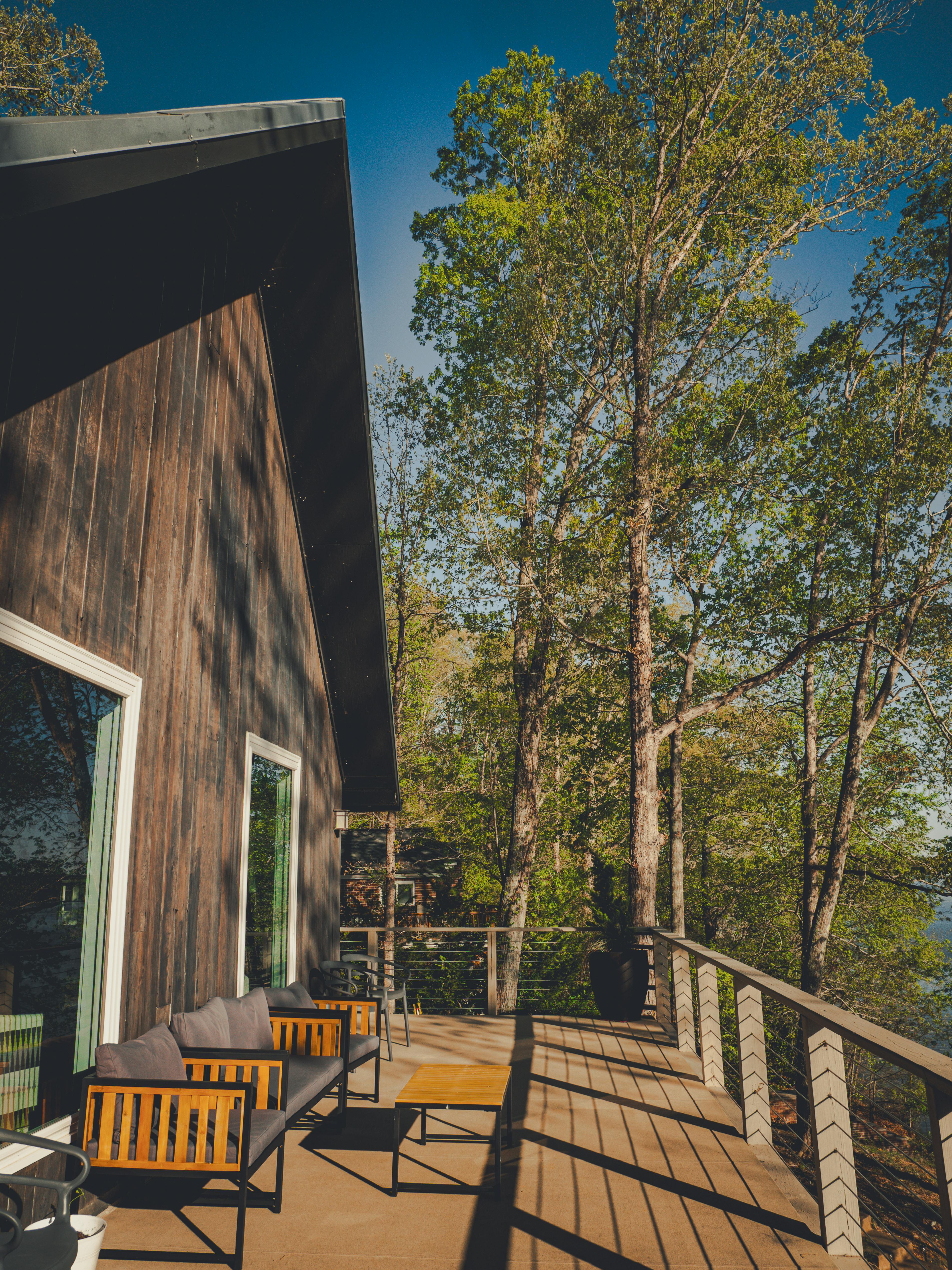 A wooden deck with chairs and a table in front of a house surrounded by trees.