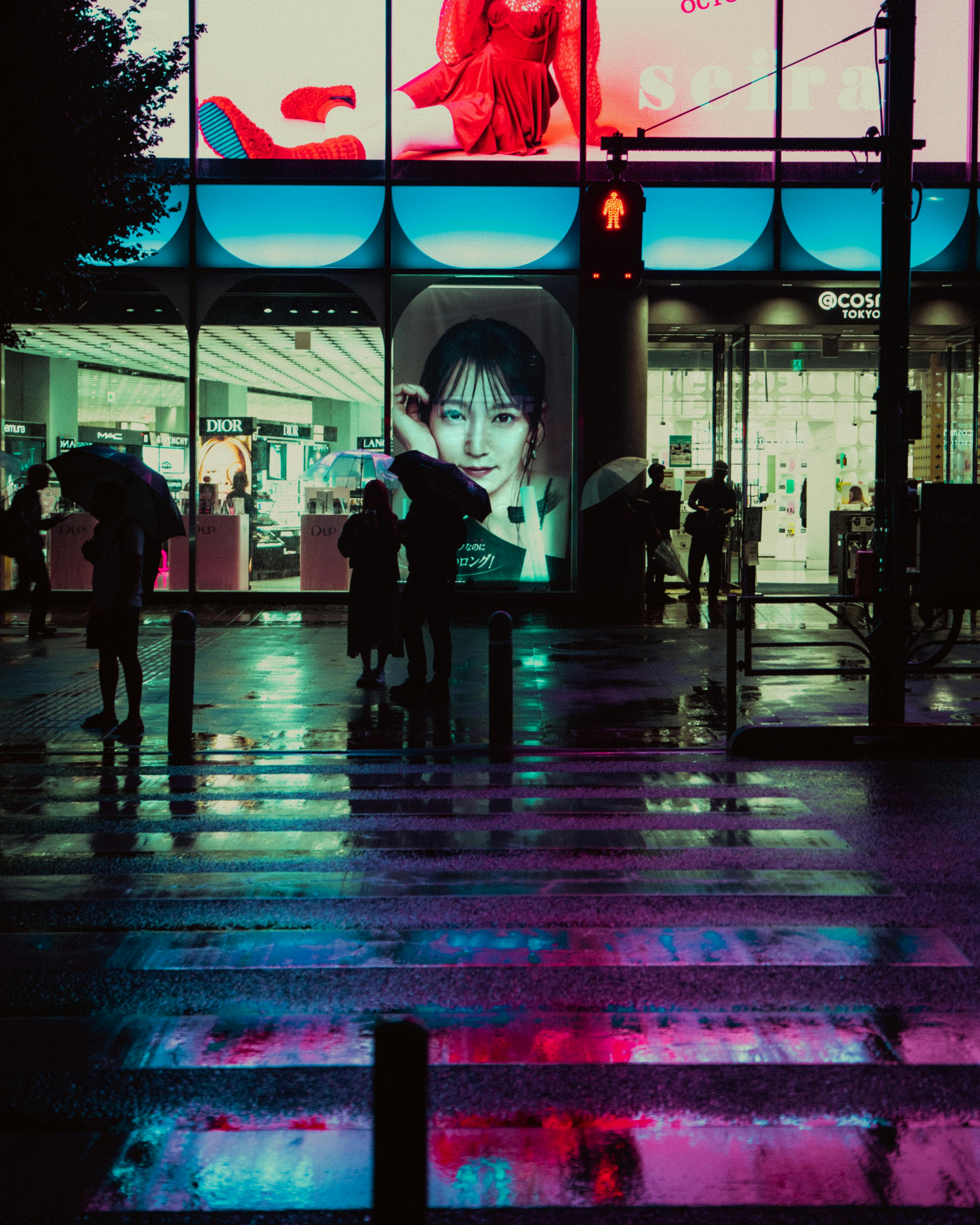 Neon-lit Tokyo street at night, showcasing people with umbrellas against a vibrant city backdrop.