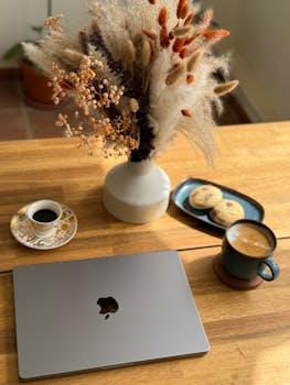 Warm, inviting workspace with laptop, coffee, and cookies on wooden table.