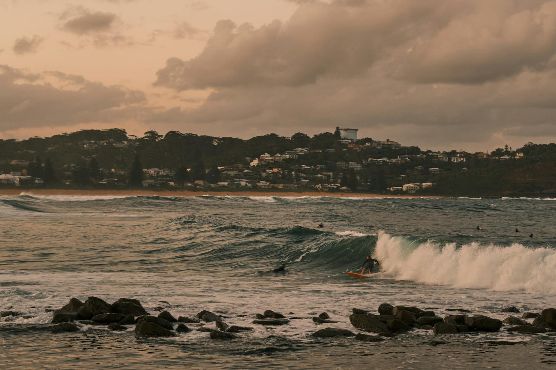 Surfers ride waves at Avoca Beach, New South Wales during a beautiful sunset.