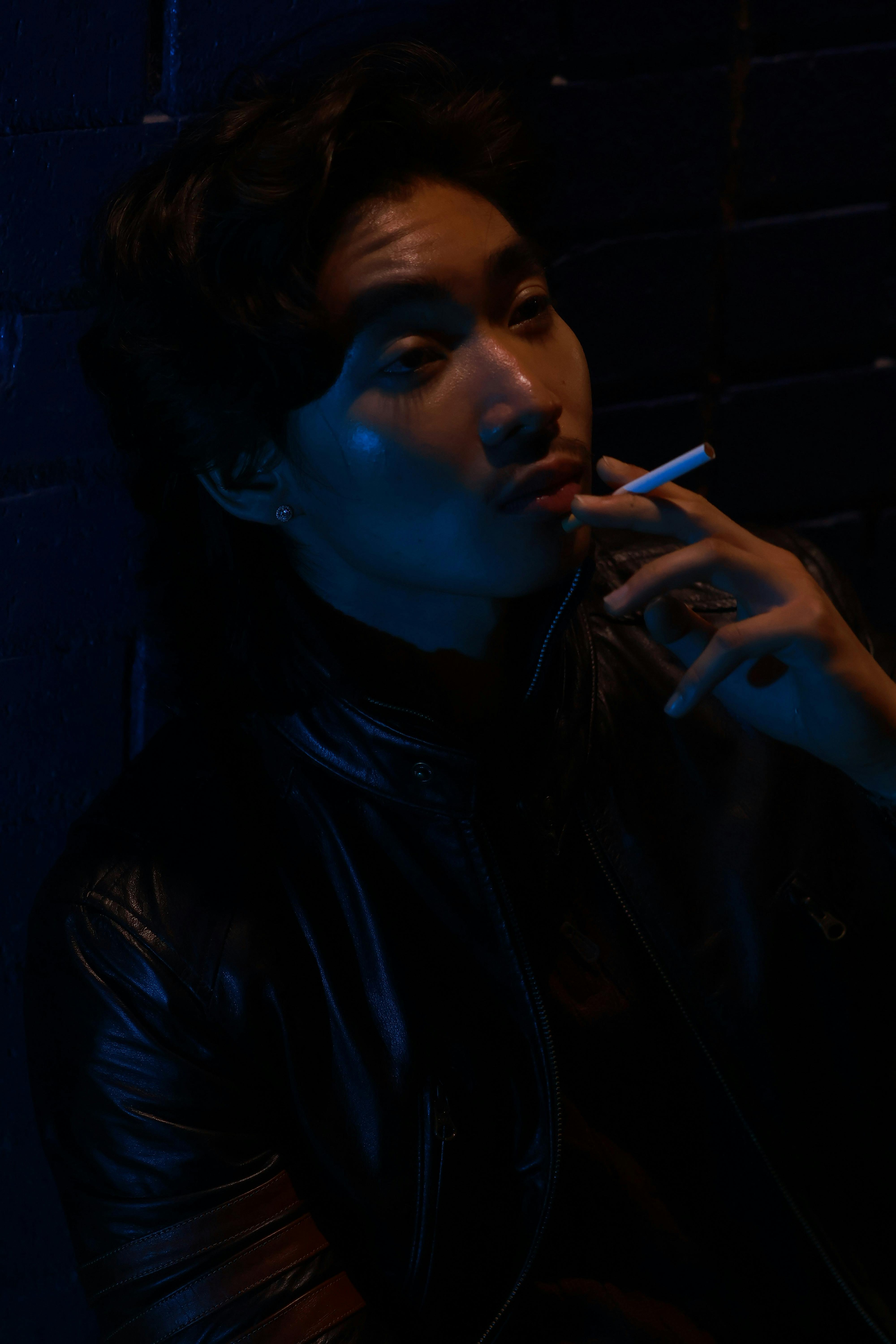 Stylish portrait of a man in a leather jacket under moody neon lighting, smoking.