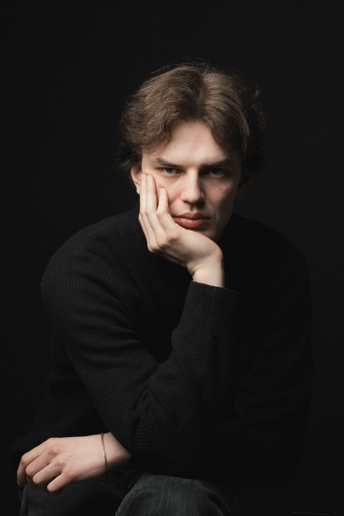 Free A young man poses thoughtfully against a dark background in a studio portrait. Stock Photo