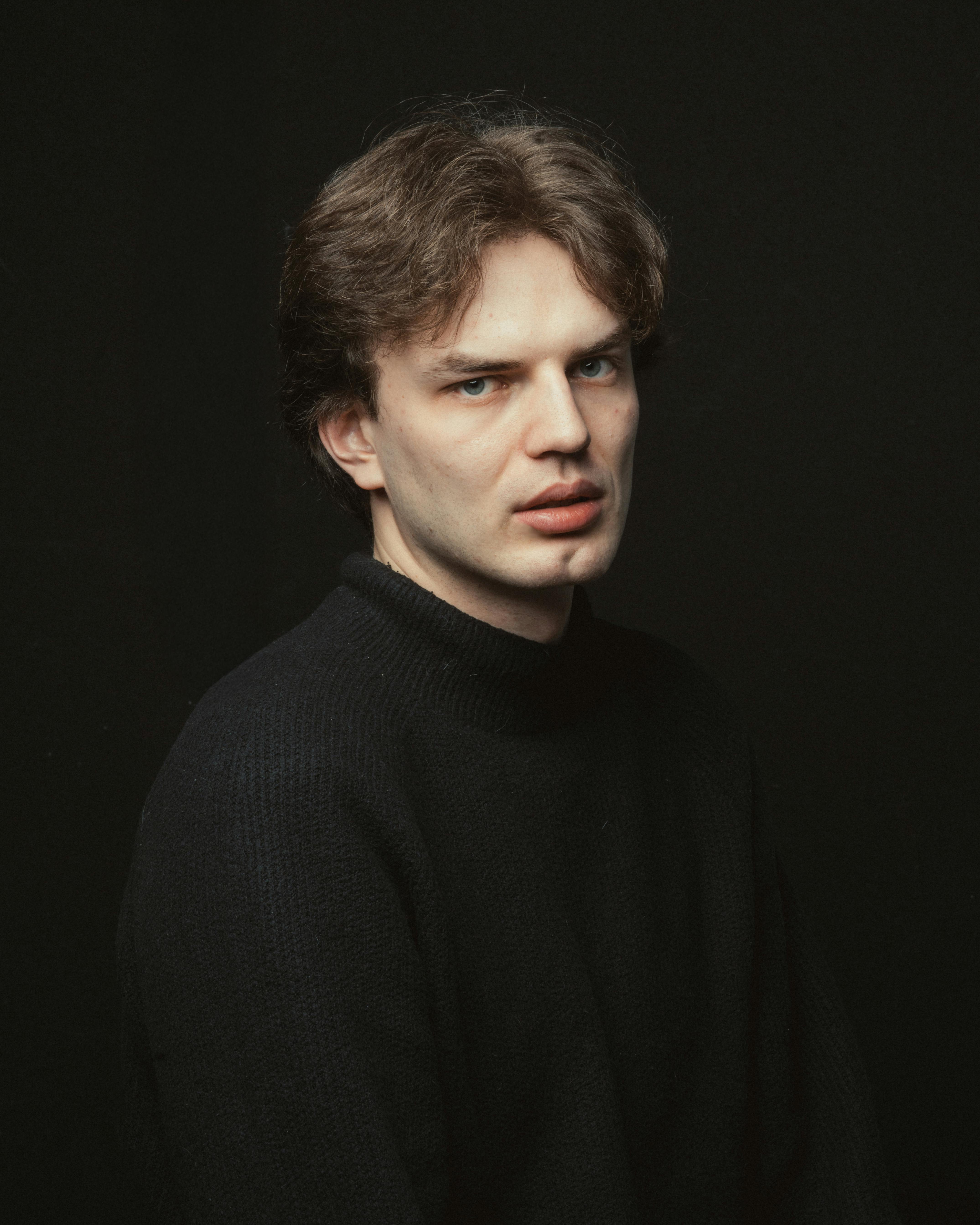 Dramatic portrait of a young man in a black sweater against a dark background.