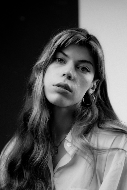 Free Artistic black and white photo capturing a young woman in a thoughtful pose wearing a white shirt. Stock Photo