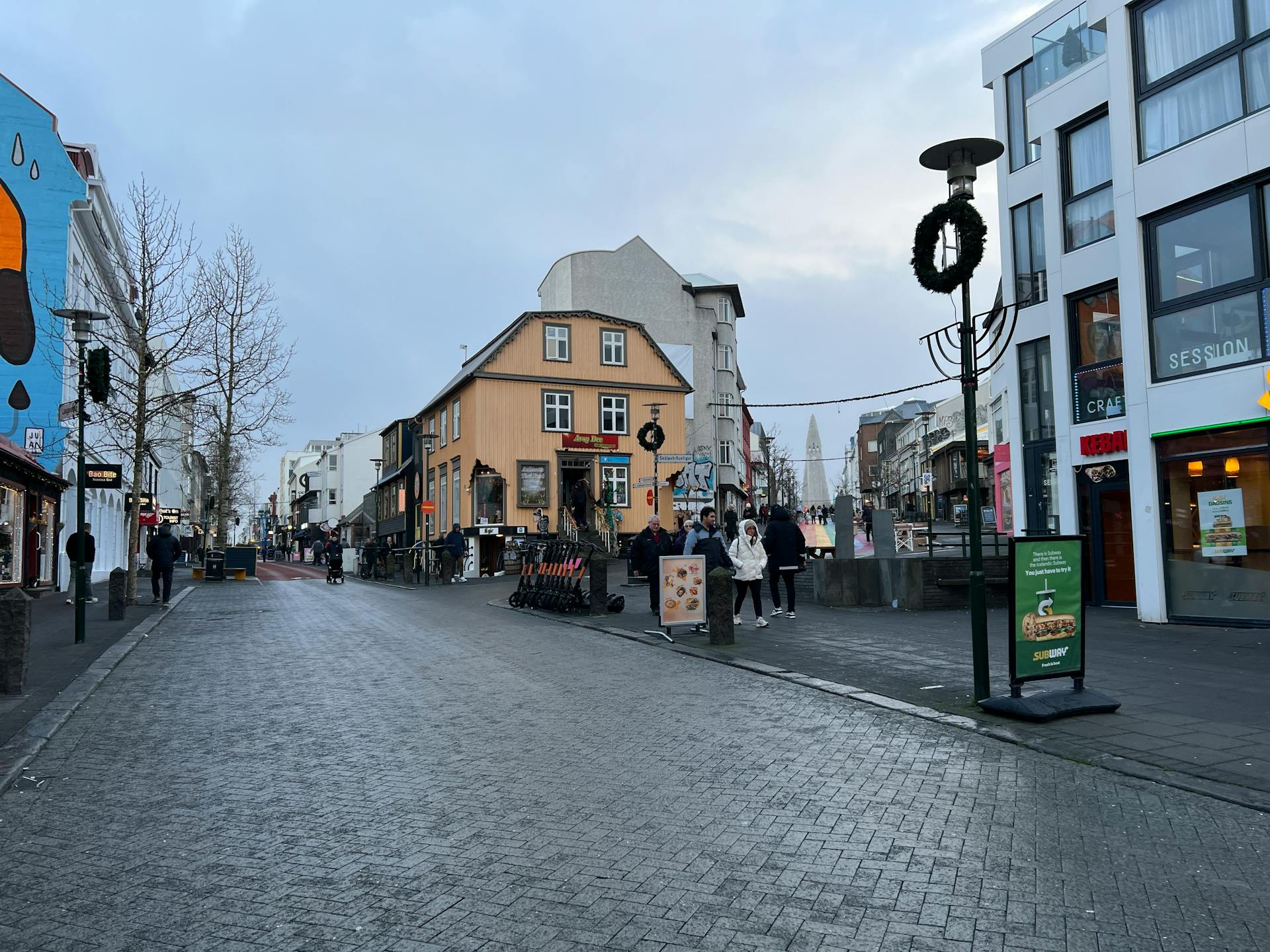 A bustling street scene on Laugavegur, Reykjavik with people and shops under an overcast sky.