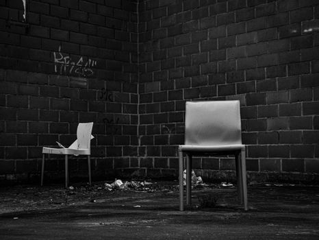 Two empty chairs in a gritty urban environment with graffiti-covered brick walls.