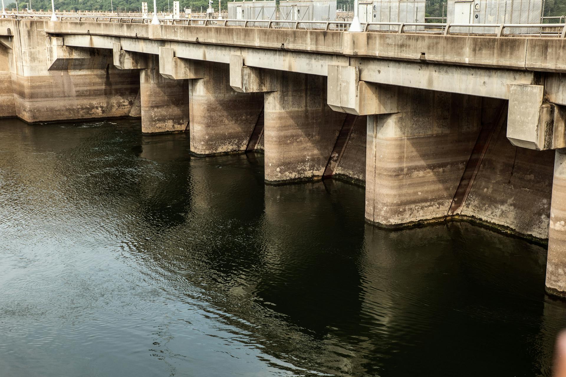 A robust concrete dam structure with reflections over a calm water surface.