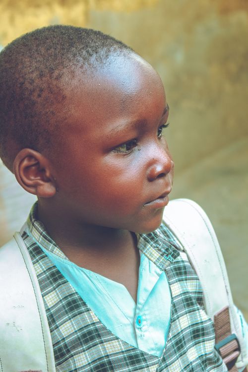 Free Young child wearing a plaid shirt and white backpack, gazing thoughtfully. Stock Photo