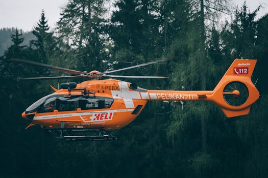 Bright orange rescue helicopter in flight over a dense forest, showcasing emergency service in action.