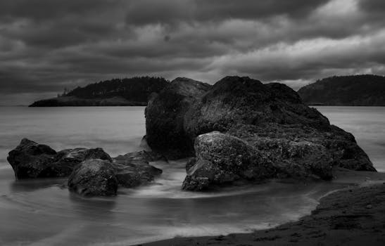 Black and white image of rugged rocks along the coastline under dramatic cloudy skies.