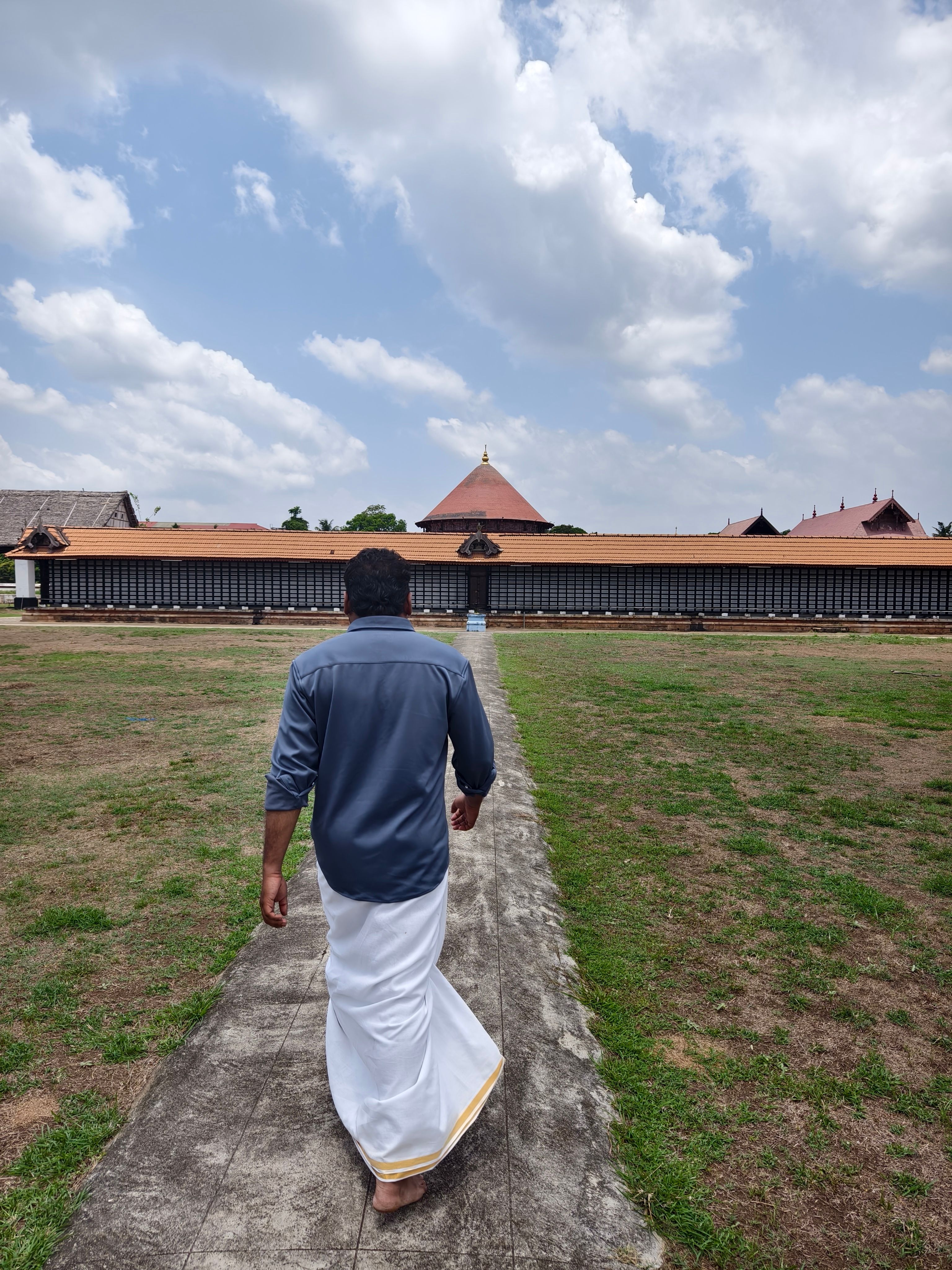 A man in traditional attire walks towards a large temple with a clear sky overhead.