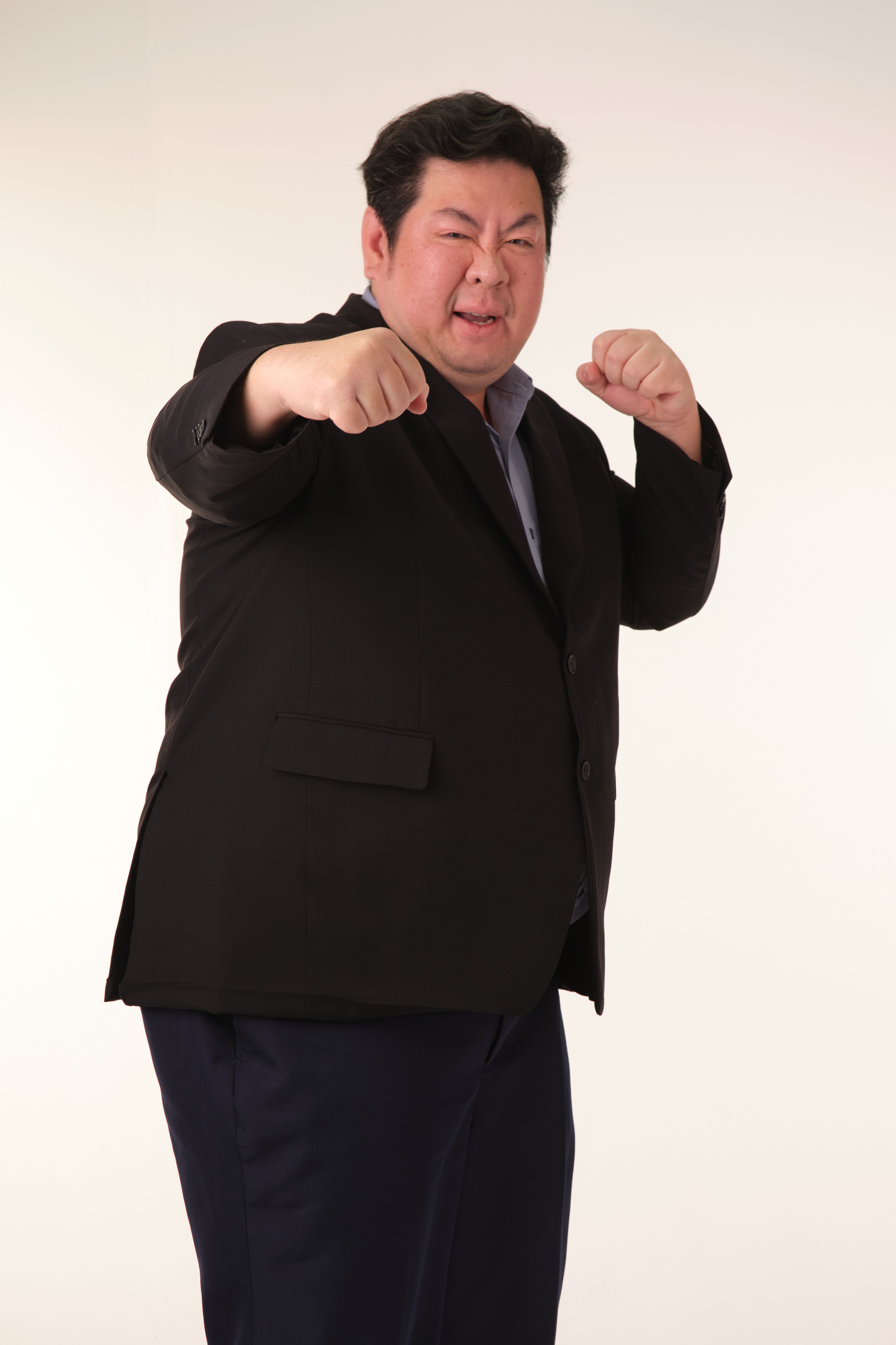 A man in a suit confidently poses in a boxing stance against a plain background.