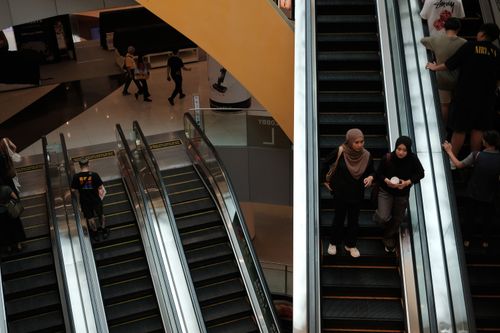 Free Daily hustle in a Singapore shopping mall, featuring busy escalators and diverse visitors. Stock Photo
