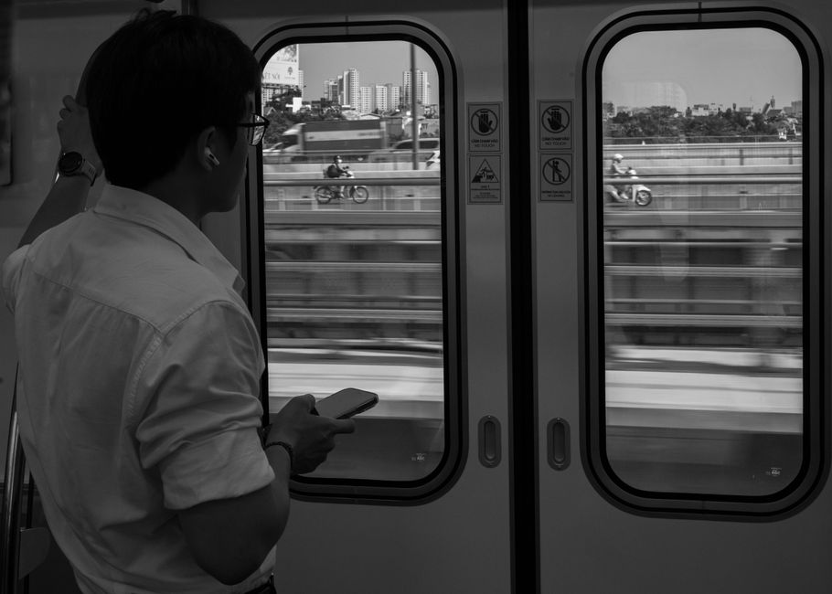 Man looking out train window at city skyline. Urban commute captured in black and white.
