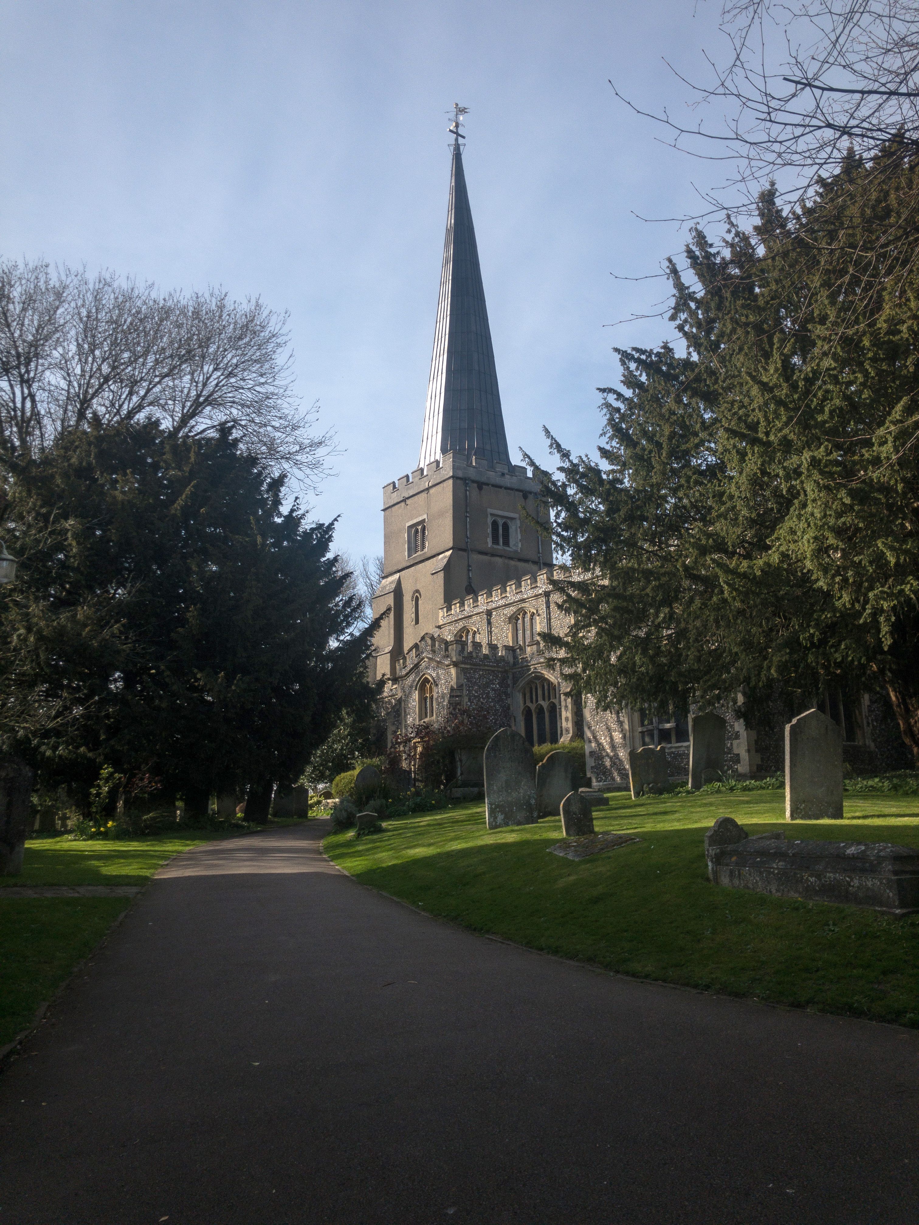 A picturesque view of St Mary's Church, Harrow on the Hill, framed by lush greenery and gravestones.