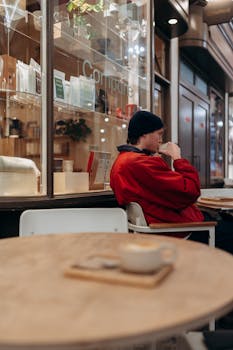 A person in a red jacket enjoys coffee at an outdoor café in London, UK.